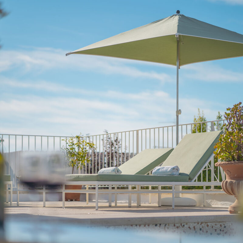 Terrazza con ombrellone verde e lettini, con una bottiglia di vino in primo piano - Palazzo Matteo