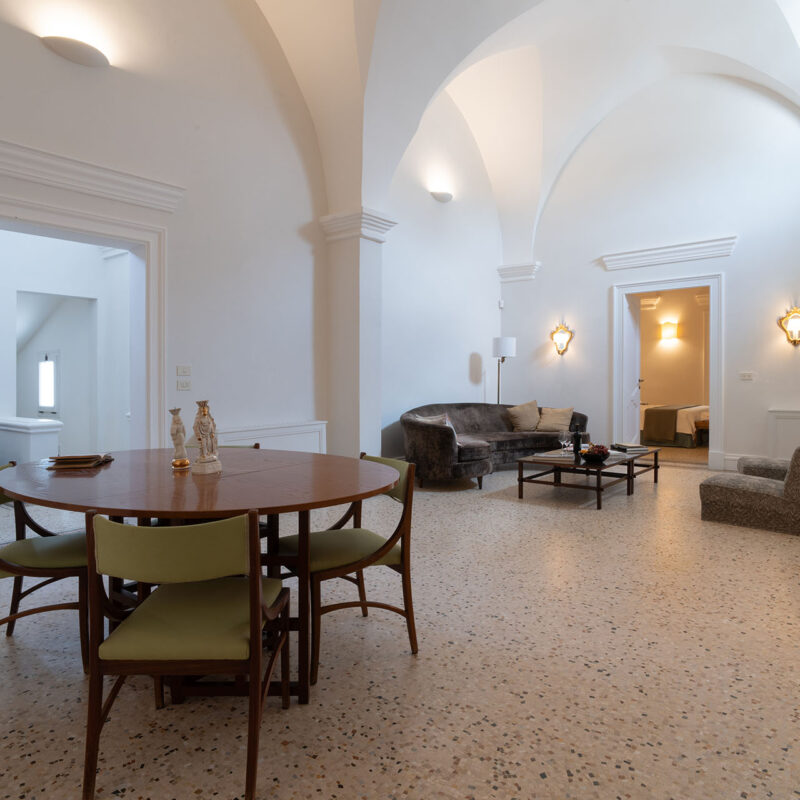 Salone con volte, tavolo rotondo con sedie verdi e salotto - Palazzo Maritati