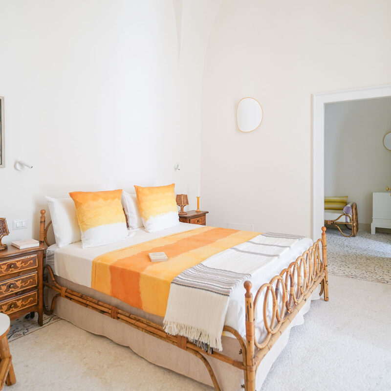 Camera con letto in rattan e coperta arancione, comodino in legno e sedia a dondolo - Casa della Vigna