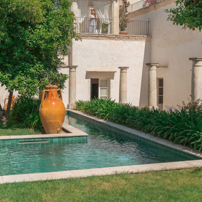 Giardino con piscina stretta, anfora in terracotta e facciata del palazzo - Palazzo Muci